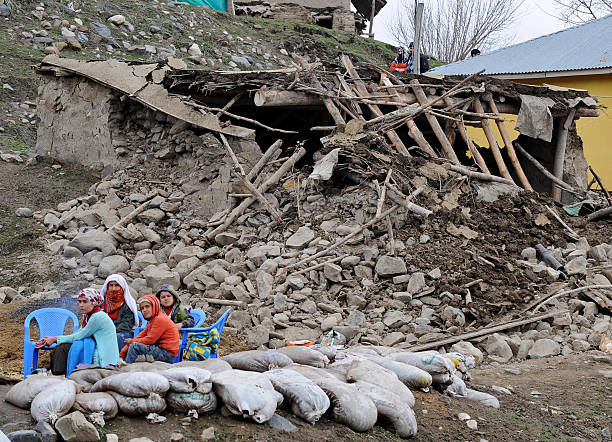 A family waits among debris in front of a destroyed house in the village of Okcular.